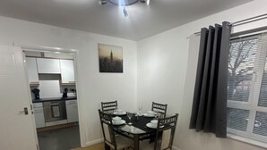 A dining area with a table set for four, a kitchen in the background, and a window with curtains. - A Home From Home (Crawley)
