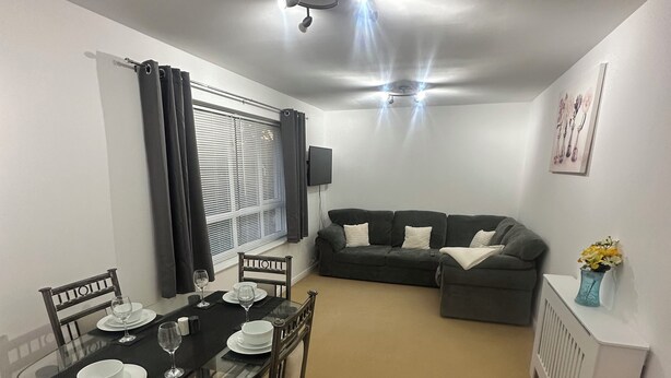 A dining area with a glass table set for four, a dark-colored sofa, and a white radiator. - A Home From Home (Crawley)