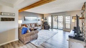 A spacious living room with a brown leather sofa, a blue throw blanket, a wooden ceiling, and a large window offering a view of buildings outside. - Balcony w/ Lake Views: Waterfront Ozarks Condo! (Osage Beach)