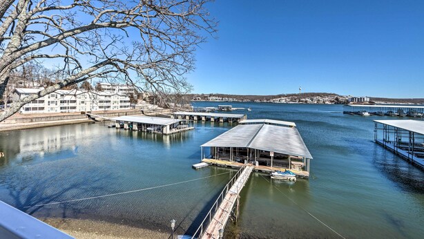 A marina with docked boats, a large building with a flat roof, and a clear blue sky. - Balcony w/ Lake Views: Waterfront Ozarks Condo! (Osage Beach)