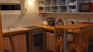 Eine kompakte Küche mit Kochinsel, eingebautem Backofen und Mikrowelle. Holzstühle und ein kleiner Mülleimer sind vorhanden.