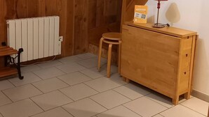 Ein Zimmer mit Holzwänden, einem Heizkörper, einem kleinen Hocker, einem Holztisch mit Lampe und einer Treppe.