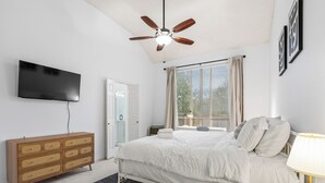 A bedroom with a bed, a ceiling fan, a TV, a dresser, and a window with curtains.