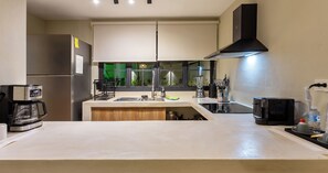 A modern kitchen with a built-in oven, a coffee maker, a sink, and a window with a view of greenery. - Casa Venado | Private Pool · Peaceful rest · Across from a Park · Parking (Mérida)