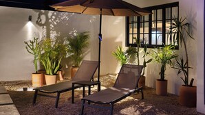 Une terrasse avec deux fauteuils, une table et plusieurs plantes en pot.