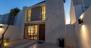 Un edificio moderno de dos pisos con un balcón, un ventanal grande y una puerta con reja de metal.