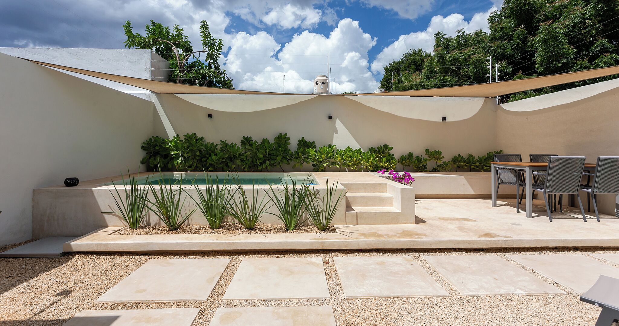 Un área de piscina exterior moderna con una mesa y sillas integradas, rodeada por un patio con mosaicos de guijarros.