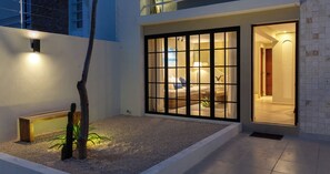 A modern house with a large sliding glass door leading to a bedroom. - Casa Venado | Private Pool · Peaceful rest · Across from a Park · Parking (Mérida)