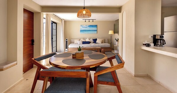 Una cocina moderna con cafetera, un comedor con mesa y sillas de madera redondas, y una sala de estar con sofá y un cuadro.
