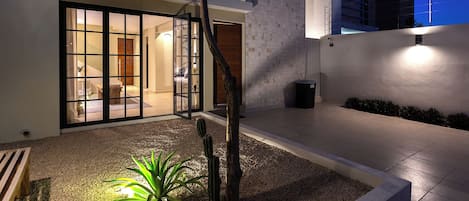 A modern house with a glass door entrance, a cactus plant, and a trash bin.