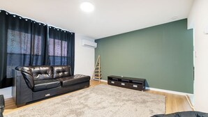 A living room with a black leather sofa, a grey shag carpet, a wooden ladder, and a built-in storage unit against a green wall. - Modern 1BR Apt Near Lake & Downtown (Sandwich)