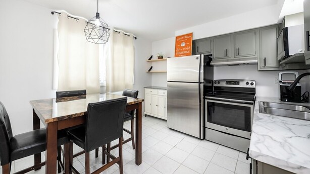 A modern kitchen with a dining area, stainless steel appliances, and a marble countertop. - Modern 1BR Apt Near Lake & Downtown (Sandwich)