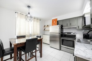 A modern kitchen with a dining area, stainless steel appliances, and a marble countertop. - Modern 1BR Apt Near Lake & Downtown (Sandwich)
