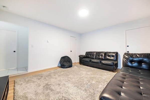 A room with a black leather sofa, a black bean bag chair, and a grey shag rug. - Modern 1BR Apt Near Lake & Downtown (Sandwich)