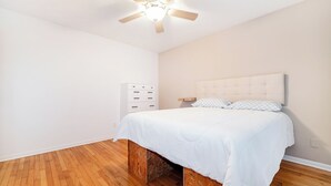 A bedroom with a bed, a ceiling fan, a white dresser, and a wooden floor. - Modern 1BR Apt Near Lake & Downtown (Sandwich)