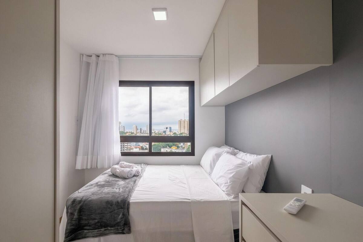 A modern hotel room with a bed, a bedside table, a window with a city view, and a curtain.