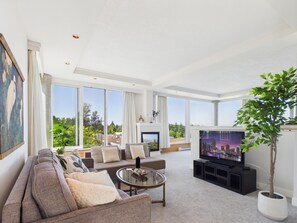 Ein modernes Wohnzimmer mit einer Sofagarnitur, einem Couchtisch, einem Fernseher und einem großen Fenster mit Blick auf die Stadt.