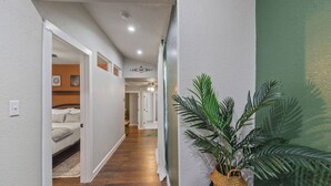 A hallway with wooden flooring, white walls, and a green accent wall. There is a potted plant on a black table. - Botanical Oasis Near Riverwalk - Sleeps 12 (San Antonio)