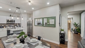 A modern kitchen with stainless steel appliances, a dining area with a wooden table set for four, and a hallway leading to another room. - Botanical Oasis Near Riverwalk - Sleeps 12 (San Antonio)