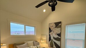 A bedroom with a bed, a ceiling fan, two windows, and a wall-mounted artwork. - The Sego Lily @ HSRV (Ivins)