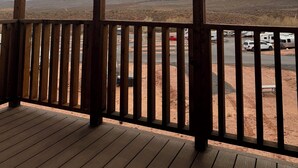 A covered outdoor area with a view of a desert landscape, wooden railings, and a paved road with vehicles. - The Sego Lily @ HSRV (Ivins)