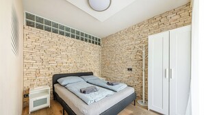 A bedroom with a stone wall, a bed with grey bedding, a white wardrobe, and a coat rack. - La Dolce Vita –Massage Shower Stay W/ Ac + Balcony (Budapest)