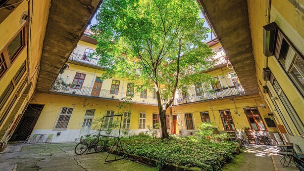 A courtyard with a tree, bicycles, and a building with balconies. - Krisztina Residence –Cozy Family Gem By Castle (Budapest)