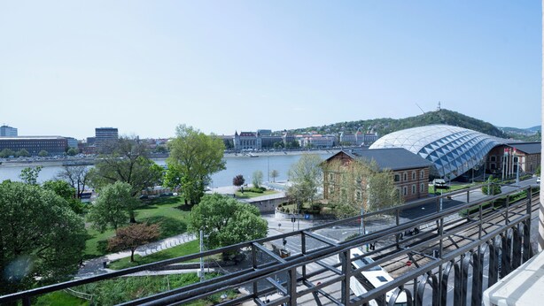 A view of a riverside area with a modern building, a bridge, and a tram line. - Aurelia Suite – Spacious W/ Ac & Danube View (Budapest)
