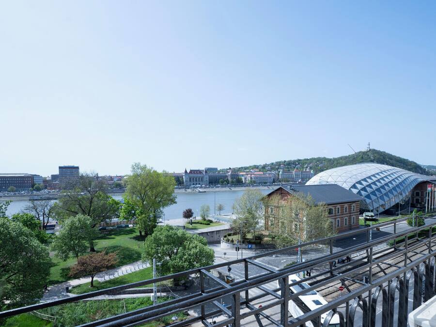 A view of a riverside area with a modern building, a bridge, and a tram line.