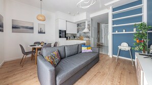 Un appartement moderne avec un canapé gris, un coin repas, une cuisine et un mur d’accent bleu.