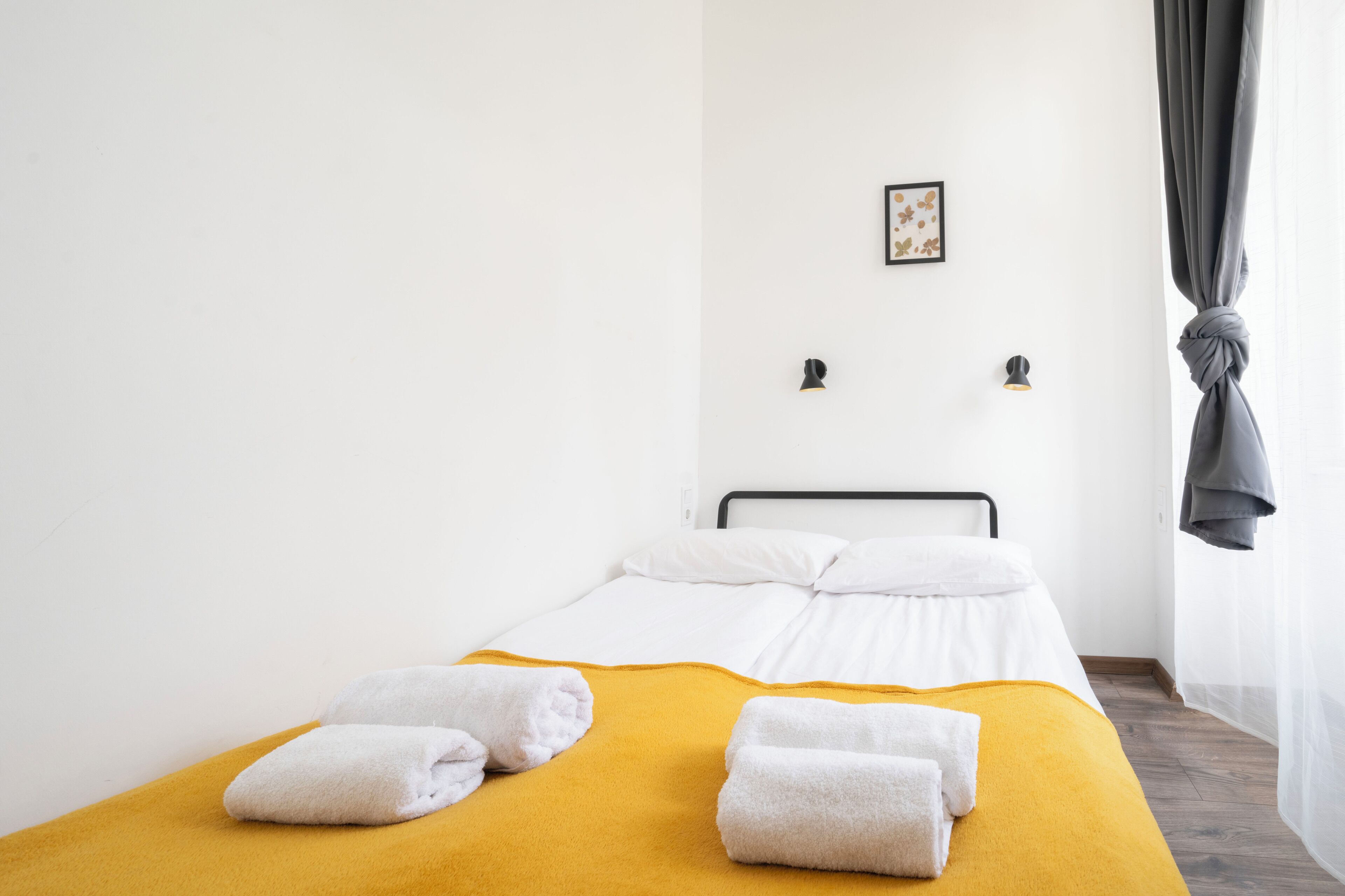 A single bed with white linens, a mustard-colored blanket, and two neatly folded towels.