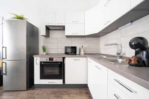 A modern kitchen with a stainless steel refrigerator, built-in oven, microwave, and a coffee maker on the counter. - The Simple Spot (Budapest)