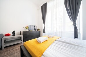 A hotel room with a bed, a desk, a dresser, and a window with curtains. - The Simple Spot (Budapest)