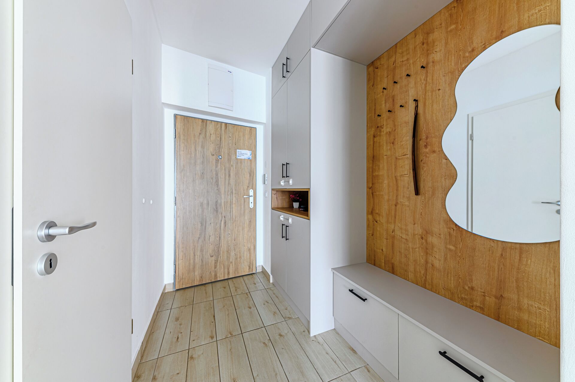 Un couloir avec une porte en bois, des armoires blanches et un grand miroir accroché au mur.