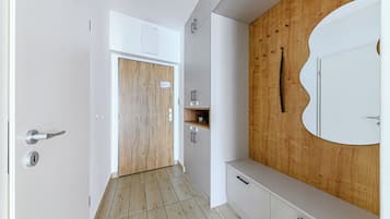 Un couloir avec une porte en bois, des armoires blanches et un grand miroir accroché au mur.