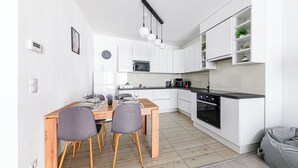 Une cuisine moderne avec des meubles blancs, une table à manger en bois et un four noir.