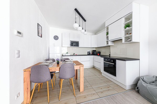 A modern kitchen with white cabinets, a wooden dining table, and a black oven. - Elite Skyview Escape (Budapest)