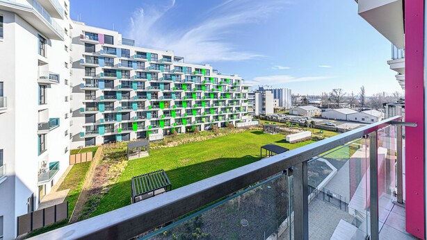 Un immeuble d’appartements moderne doté de balcons, d’une cour verdoyante et offrant une vue sur un ciel dégagé.