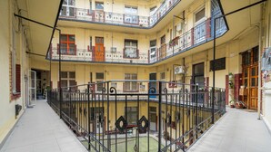 Ein mehrstöckiger Innenhof mit einer zentralen offenen Fläche, umgeben von Balkonen mit Geländern.