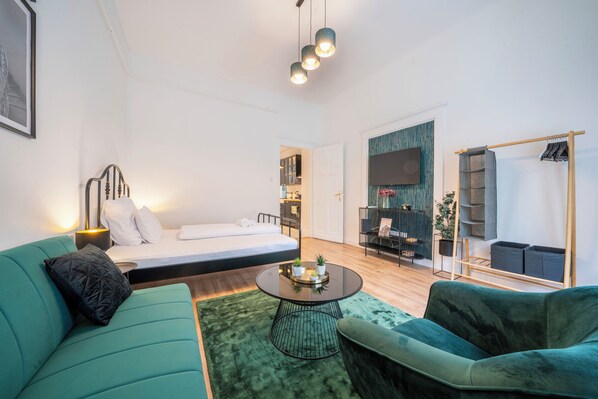 A modern room with a bed, a green sofa, a round table with plants, and a wardrobe with hanging space.