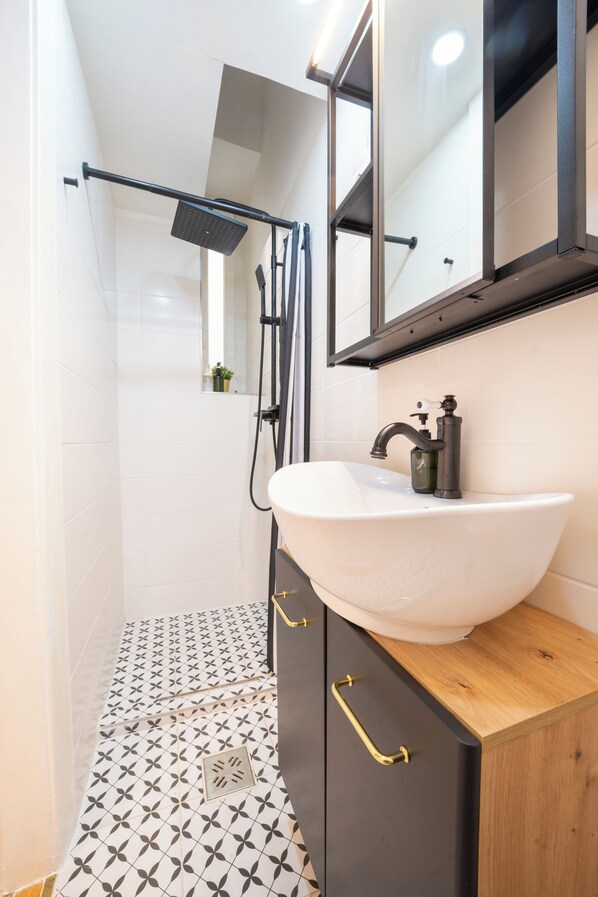 A modern bathroom with a white sink, black cabinet, and a shower area. - Green Greguss Apartment (Budapest)
