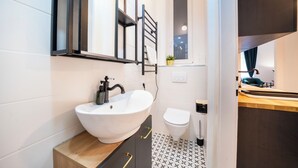 Ein modernes Badezimmer mit einem weißen Waschbecken, einem schwarzen Handtuchhalter und einem kleinen Fenster.