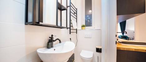 A modern bathroom with a white sink, black towel rack, and a small window.