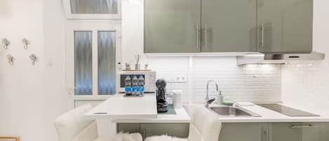 Una cocina moderna con armarios blancos, encimera blanca, un lavamanos y una cafetera.