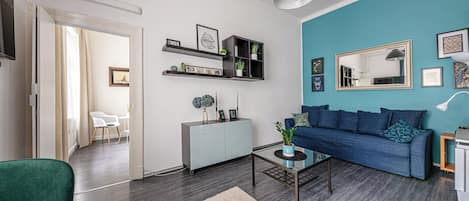 A modern living room with a blue accent wall, a grey sofa, a white cabinet, and a glass coffee table.