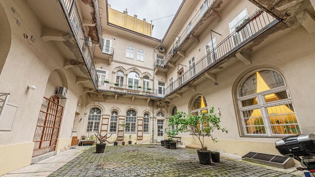 A courtyard with cobblestone flooring, potted plants, and a car parked on the right. - Chain Bridge (Budapest)