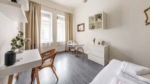 A hotel room with a bed, a desk, a chair, a dresser, a mirror, and a window with curtains. - Chain Bridge (Budapest)