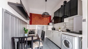 A compact kitchen with a washing machine, a dining area with chairs, and a patterned wall. - Chain Bridge (Budapest)
