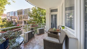 Een balkon met rieten meubilair, plantenbakken en uitzicht op gebouwen en bomen.