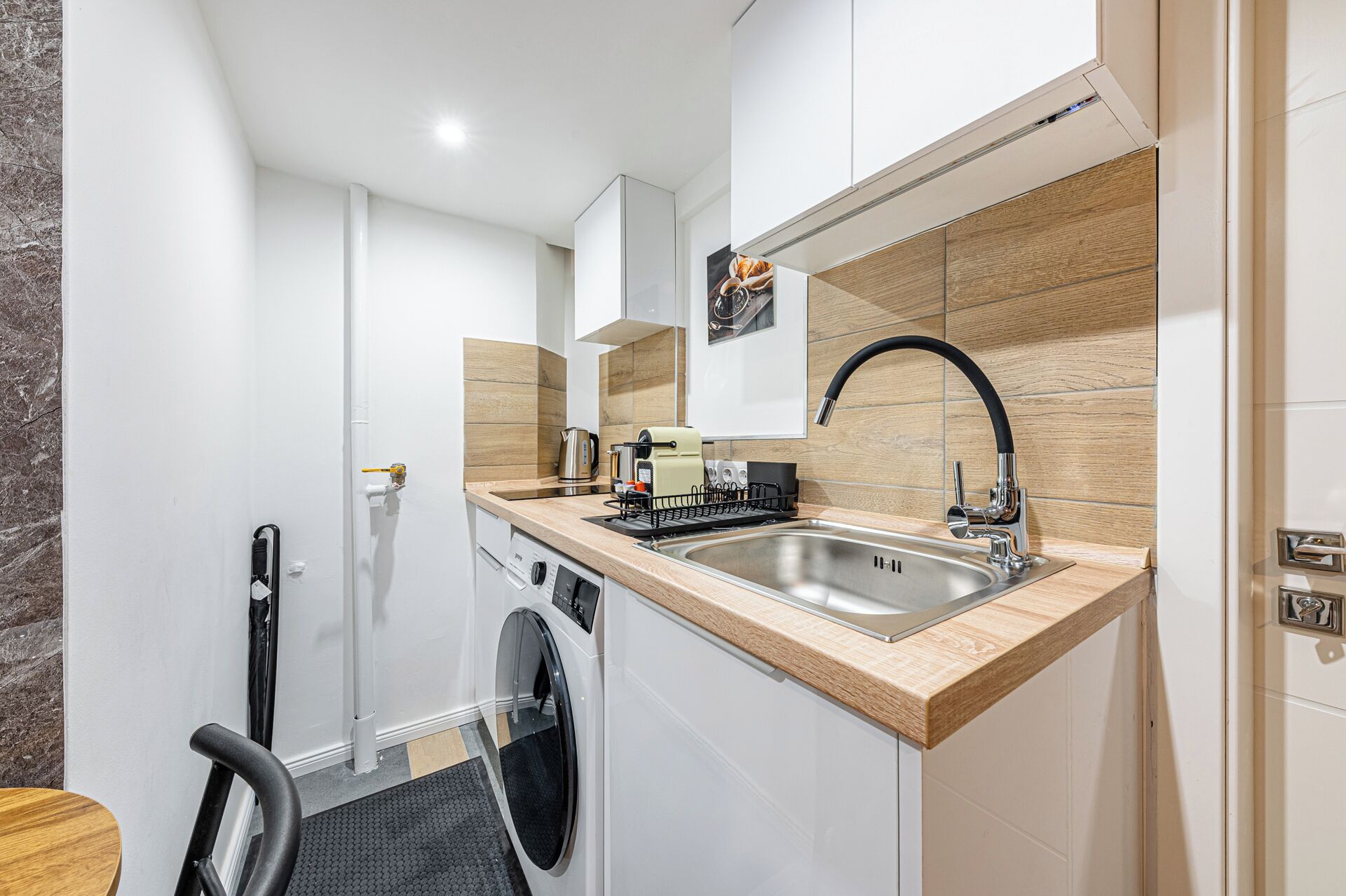 A compact kitchen with a built-in washing machine, a sink, and a coffee machine.